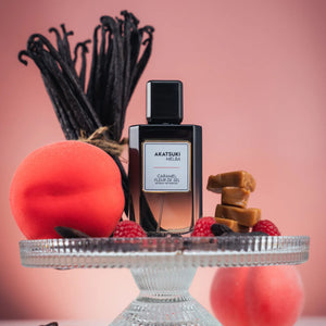 Parfum Akatsuki Melba de Fomowa Paris posé sur un présentoir avec fruits, caramel et gousses de vanille, illustrant son univers gourmand et fruité