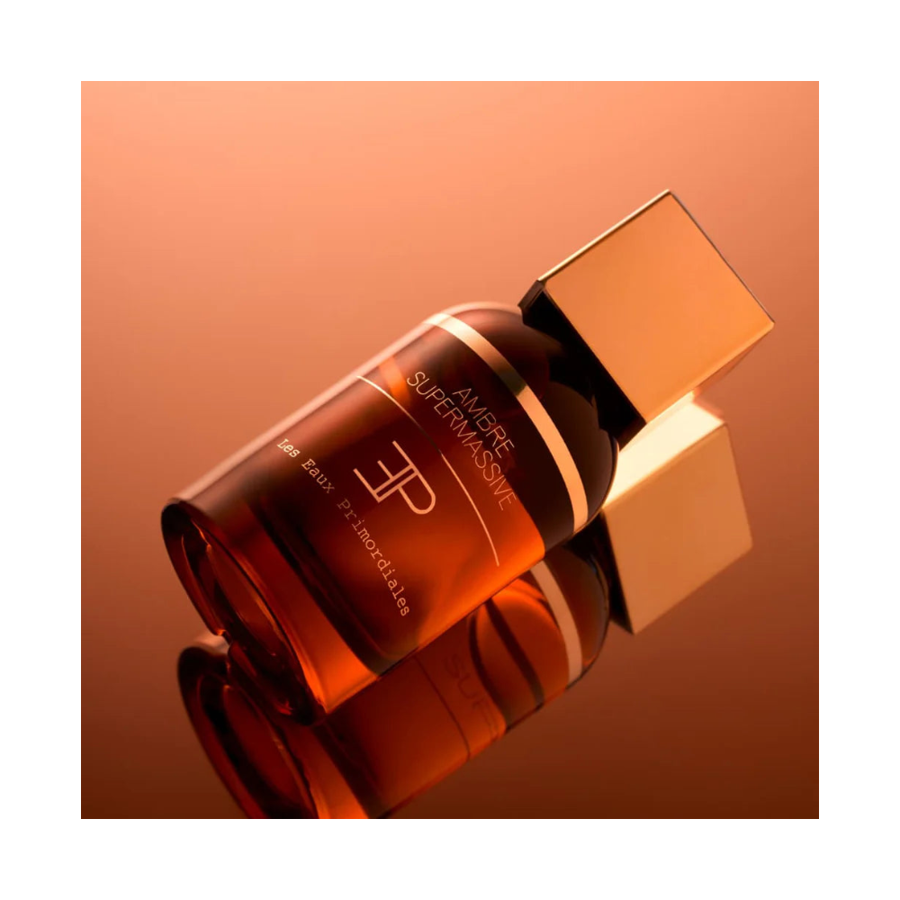 Parfum Ambre Supermassive de Les Eaux Primordiales photographié en ambiance chaude, flacon ambré aux reflets profonds