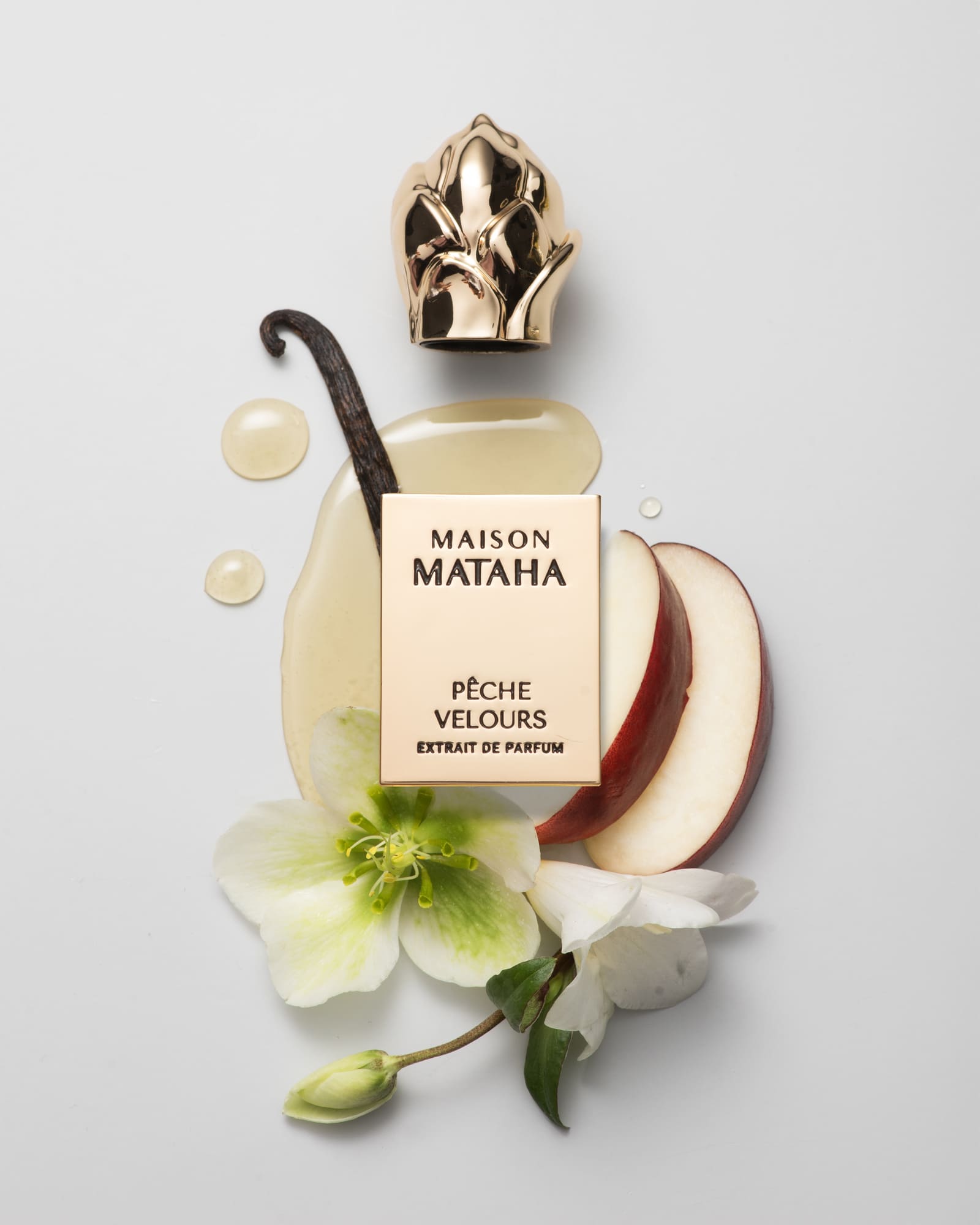 Flacon du parfum Pêche Velours de Maison Mataha entouré de tranches de pêche, de fleurs blanches et d’une gousse de vanille sur fond clair, symbolisant la douceur veloutée du parfum.